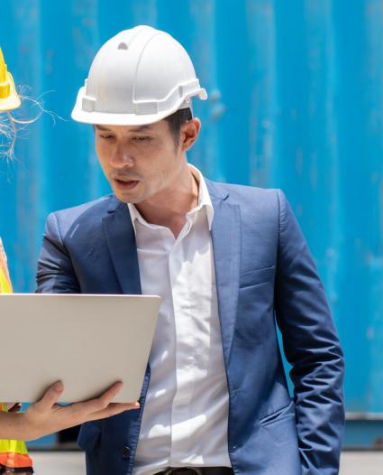 two people looking at a laptop wearing hardhats 
