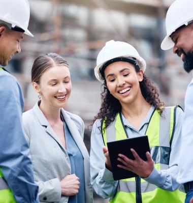 people looking at a clipboard while wearing hard hats and high visibility vests smiling