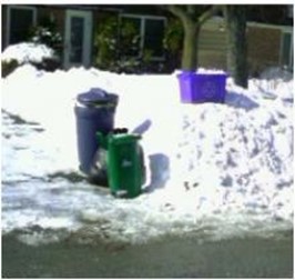 Garbage and recycling bins sitting in and around the snow on the side of the curb.