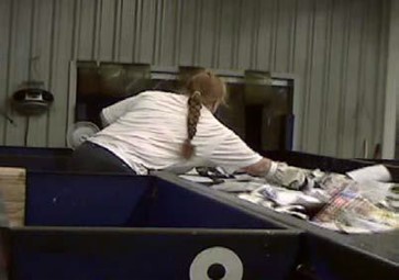   Woman leaning across conveyor to sort recycling