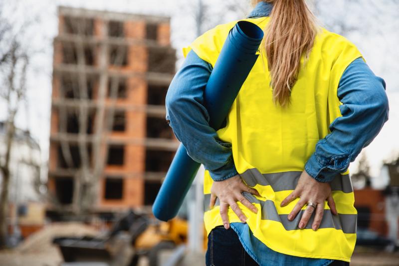 woman on construction site holding her back to show it is in pain