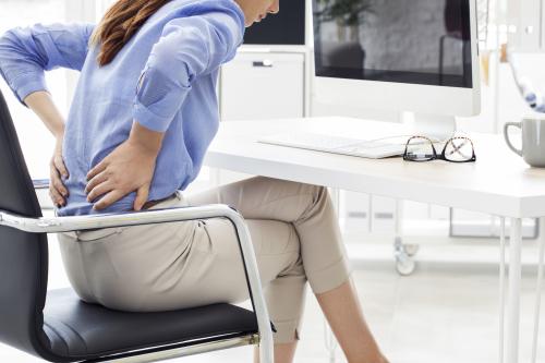 woman sitting on an office chair with her hands on her low back to indicate pain