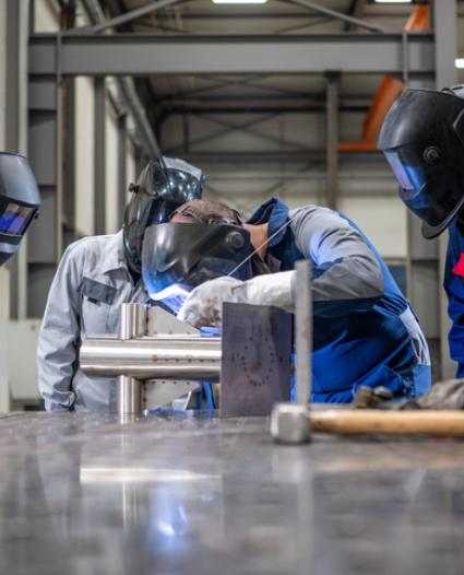 5 welders in a shop working, one with a flexed back and neck