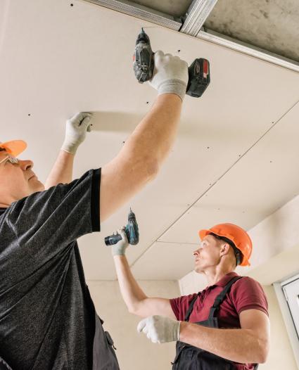 two building construction workers drilling into the ceiling (overhead work)