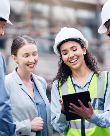 people looking at a clipboard while wearing hard hats and high visibility vests smiling