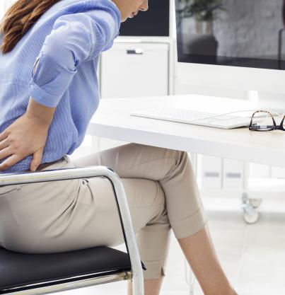 woman sitting on an office chair with her hands on her low back to indicate pain