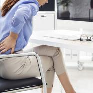 woman sitting on an office chair with her hands on her low back to indicate pain