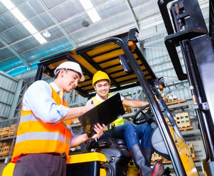 two people talking, one is sitting on a forklift