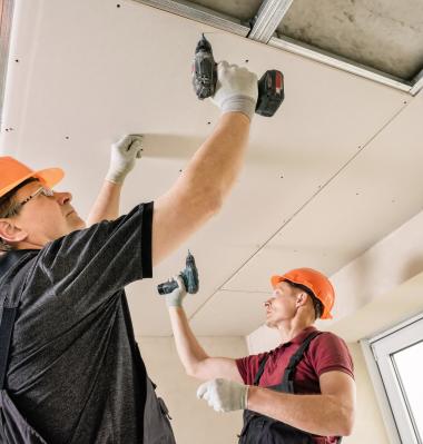 two building construction workers drilling into the ceiling (overhead work)