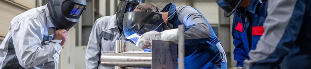 5 welders in a shop working, one with a flexed back and neck