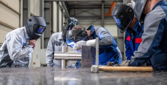 5 welders in a shop working, one with a flexed back and neck